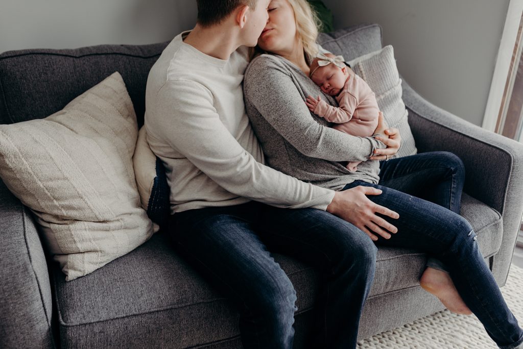 mom and dad snuggling newborn during session on couch